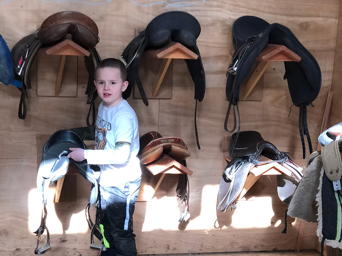 Child holding saddle in tack room.